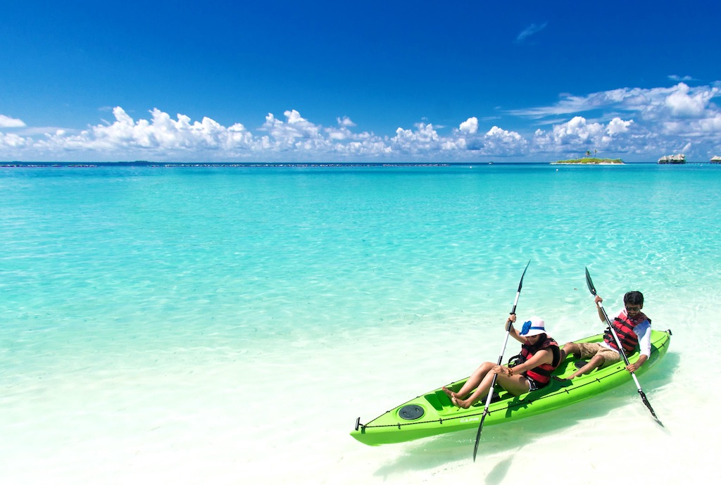 A couple paddling a green sit-on-top kayak in the blue ocean