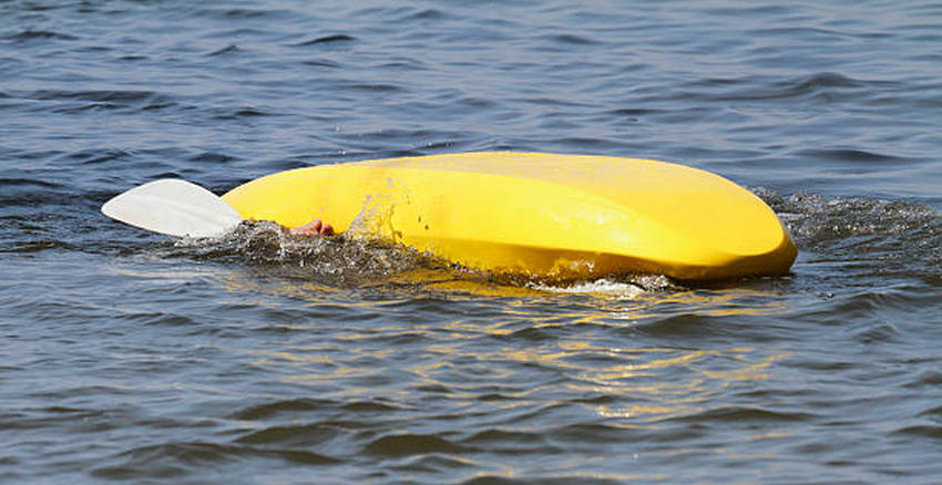 A human hand seen under a capsized yellow kayak in the sea