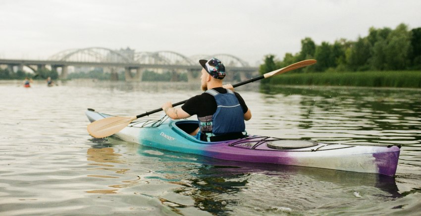 A man paddling a long kayak with  white, turquoise and lilac shades in its color on the river