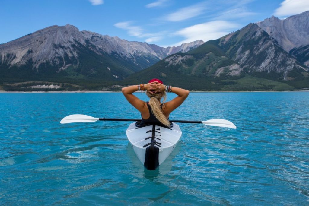 A girl in a white kayak in the blue water observes picturesque mountain scenery