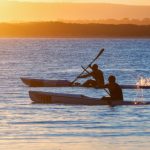 Two men paddling kayaks outlined against the sunset