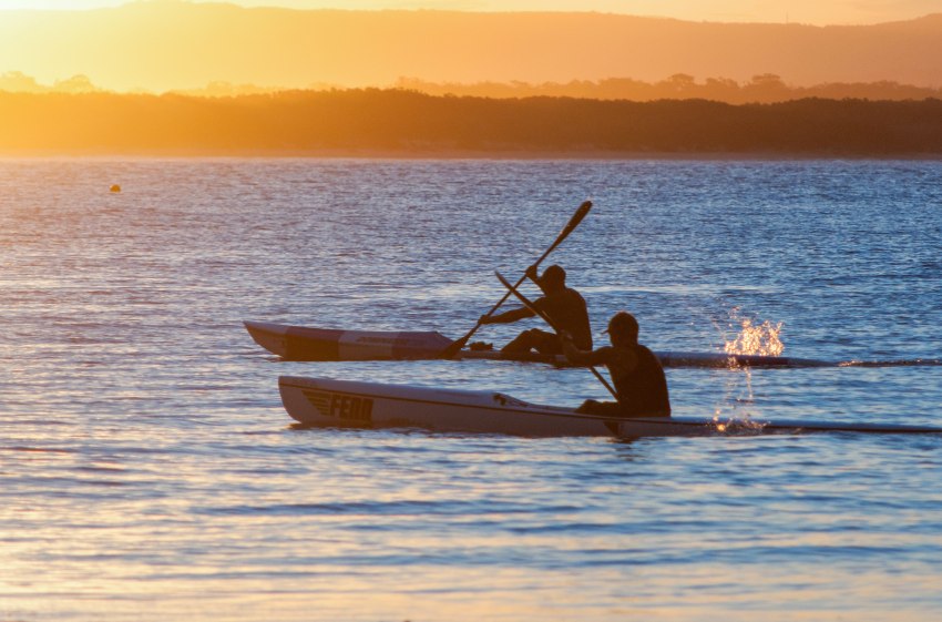 Two men paddling kayaks outlined against the sunset