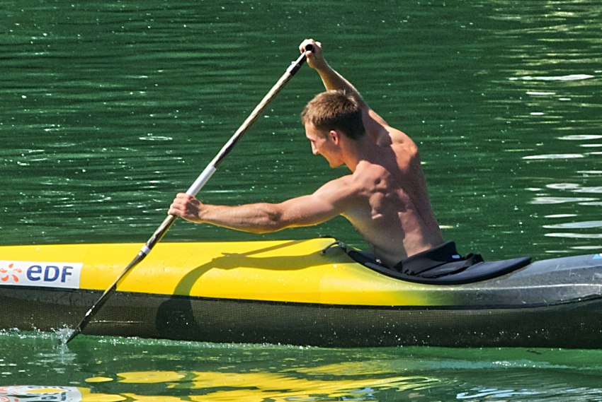 A muscled man paddling a yellow kayak