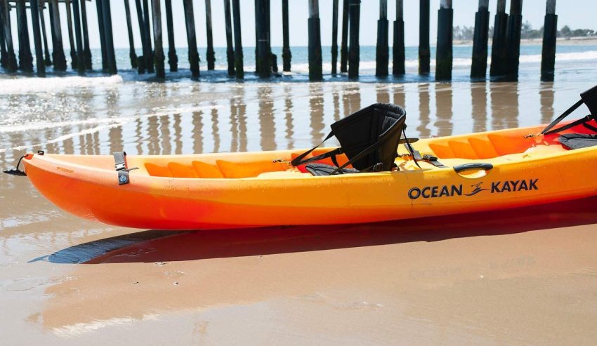 An orange kayak with two black seats on the seashore