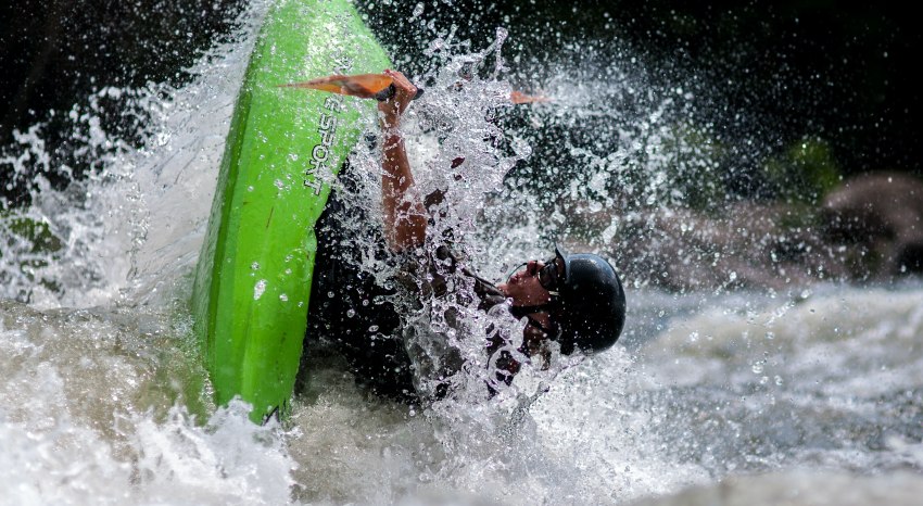 A man in a green kayak flipping in the whitewater 