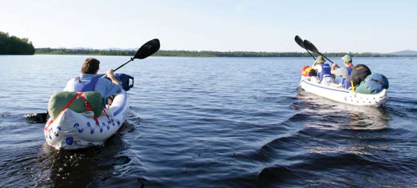 Two white inflatable kayaks with paddlers and cargo on the lake