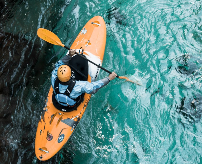 A man in an orange kayak paddling in blue waters