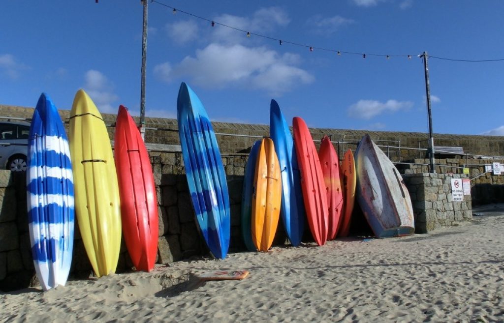 Several kayaks of various colors leaning against the stone wall