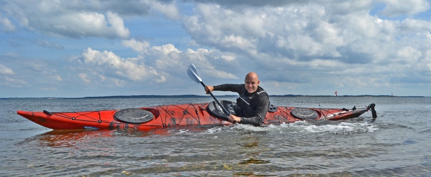 A male paddler tilting his red kayak on the water