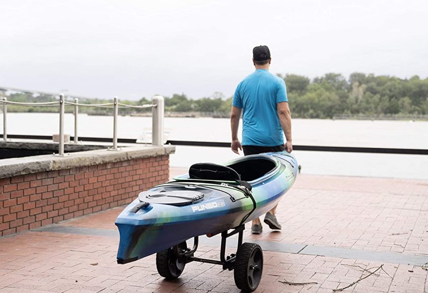 A man dragging a cart with a blue-green kayak towards the water