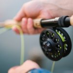 Two human hands holding a fly fishing rod with a reel
