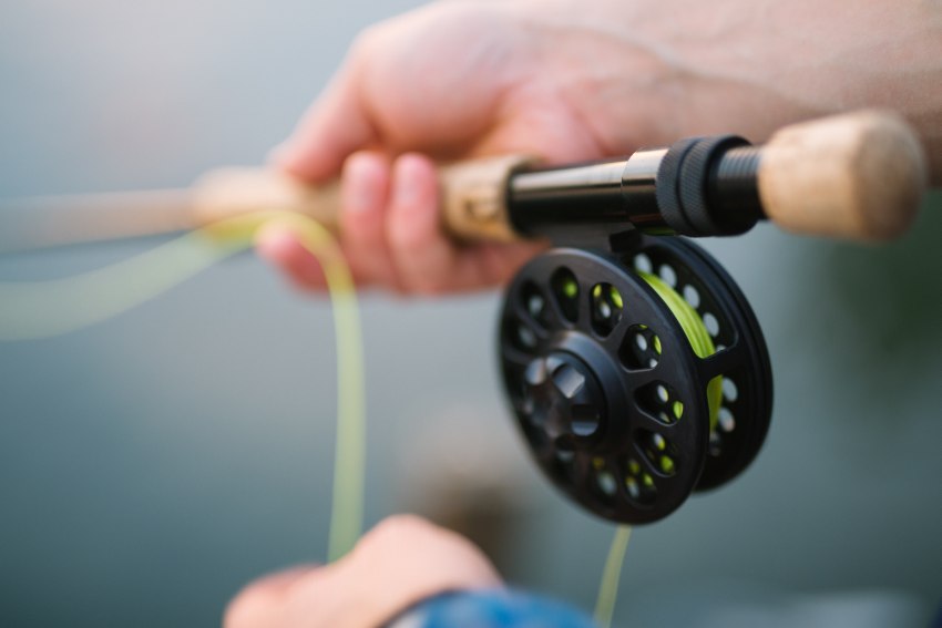 Two human hands holding a fly fishing rod with a reel