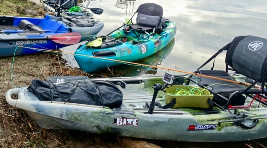 Three kayaks with various fishing equipment on the shore