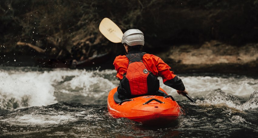 A man in an orange dry suit paddling an orange kayaks in the whitewater