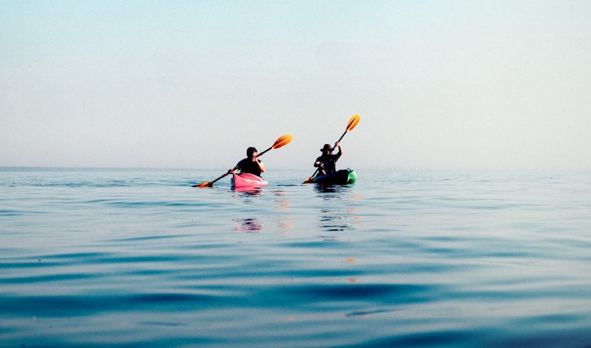 Two men paddling their kayaks in the open sea