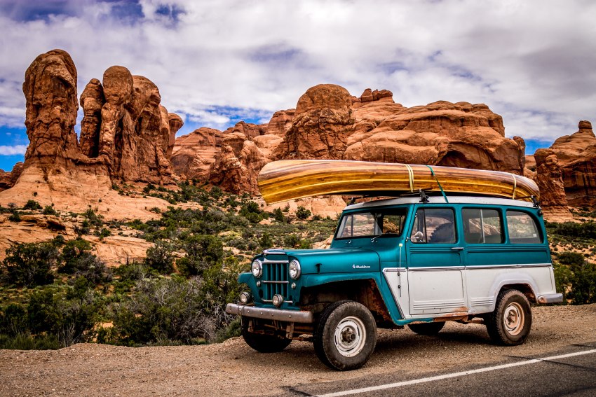 A blue-white off-road vehicle with a boat on the roof standing against the canyon scenery