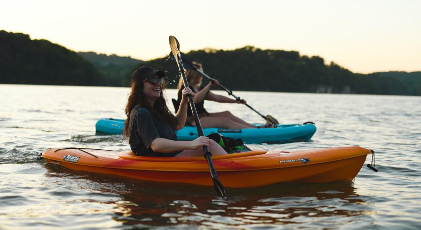 Two young ladies paddling small kayaks (orange and blue) on the water