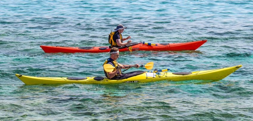 Two men paddling their long kayaks (yellow and red) offshore
