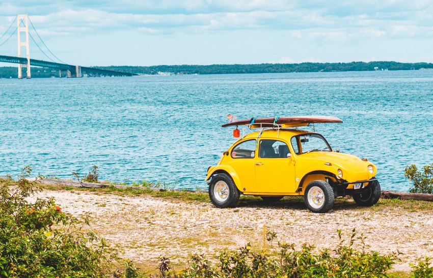 A small yellow car with a SUP board on the roof parked on the sea shore