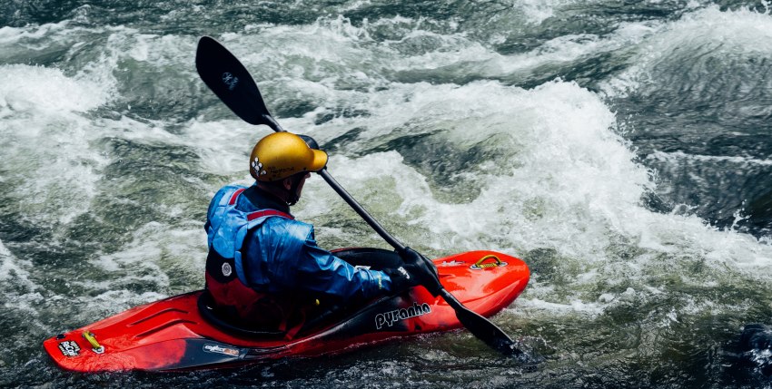 A man paddling a small red kayak in the whitewater