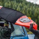 Two men loading a red kayak on a car roof