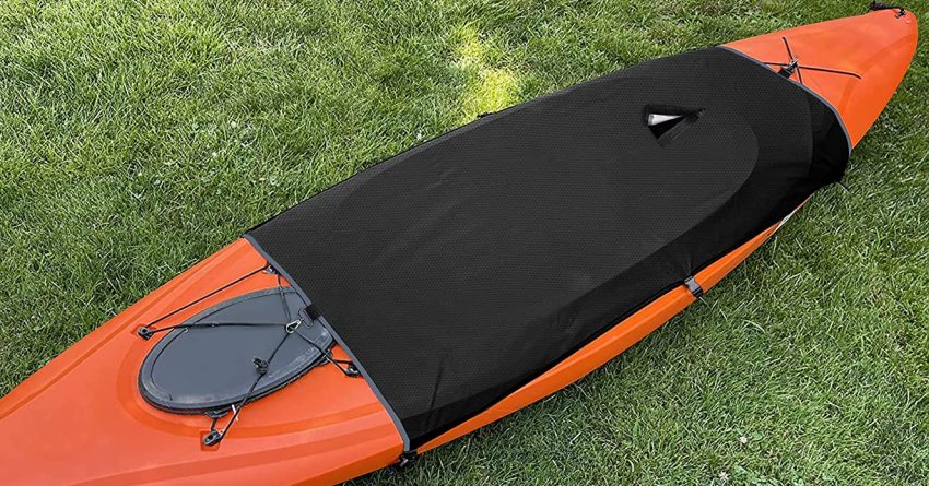 An orange kayak with a black cockpit drape resting on the grass