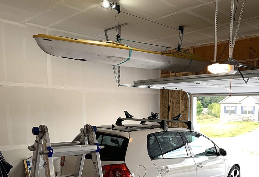 A white and yellow kayak hoisted above a white vehicle inside a garage