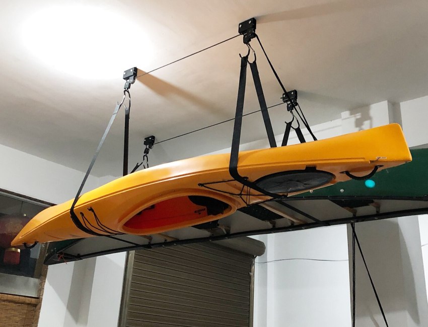A yellow kayak and a green canoe lifted by two ceiling hoists