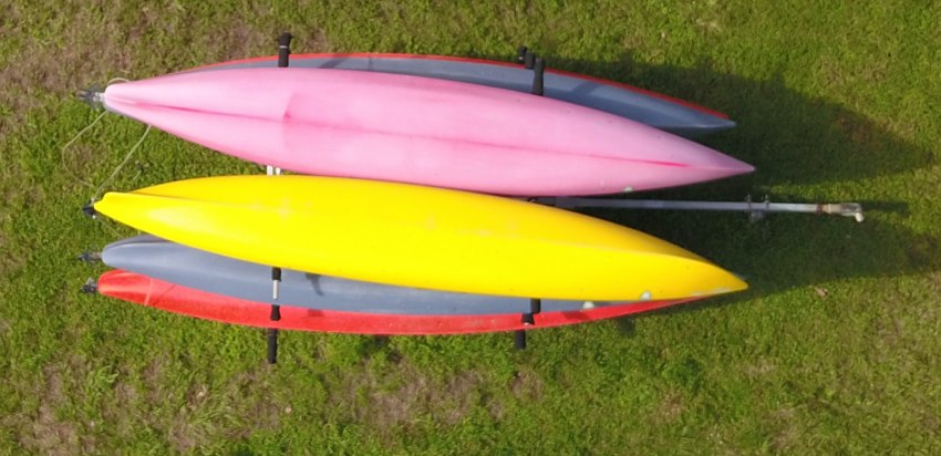 Several kayaks of different colors stacked on a trailer