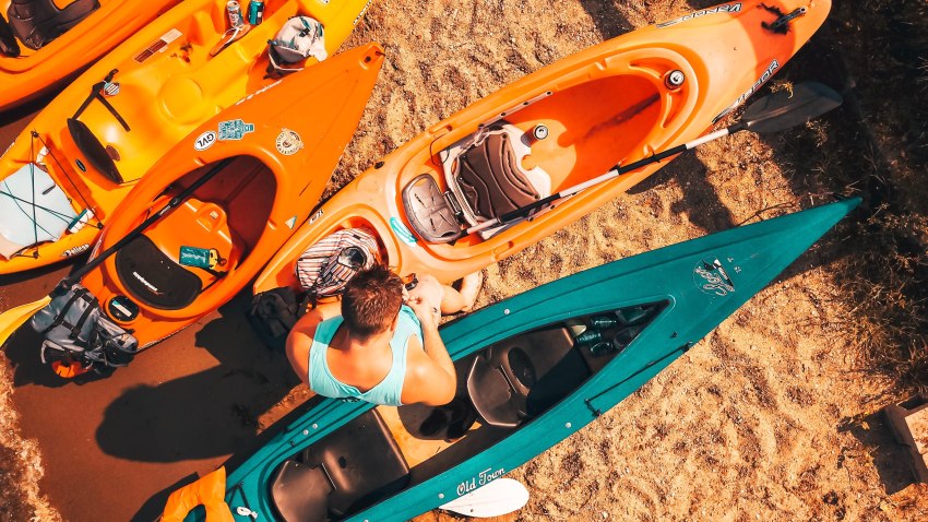 A man standing among kayaks of various sizes and colors on the beach