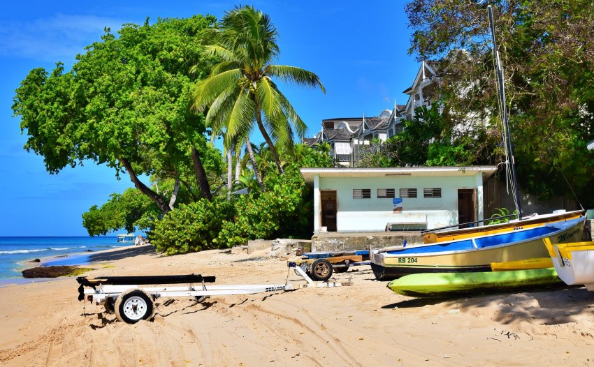 A white kayak trailer and several boats of different colors on the sea shore