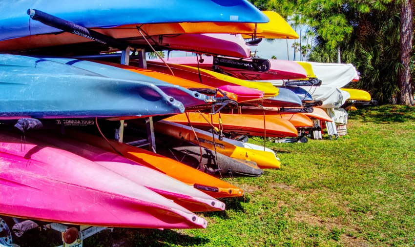 Multiple kayaks of different colors stacked on kayak trailers
