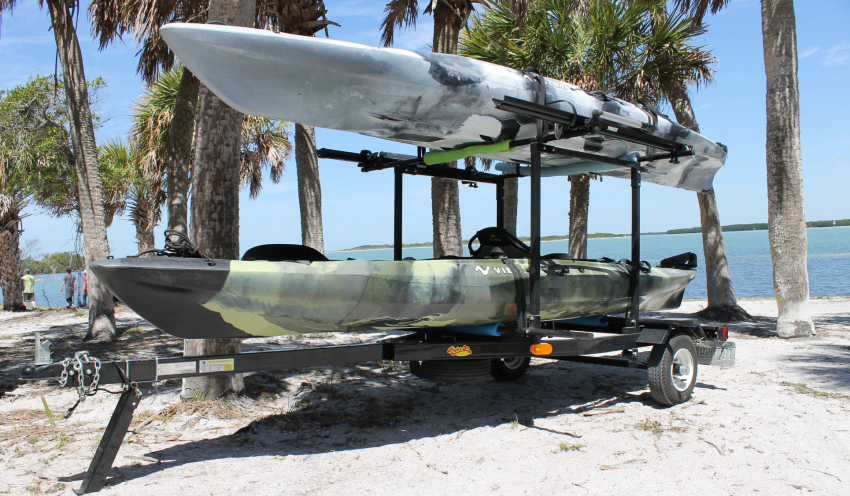 Two kayaks resting on a trailer under the palm trees near the sea