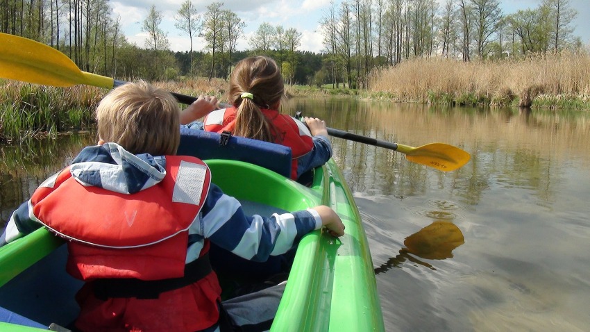 A boy and a girl paddling a green kayak in the outdoors