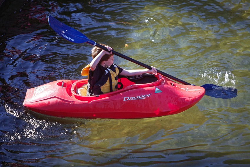 A boy in a yellow life vest paddling a small red kayak