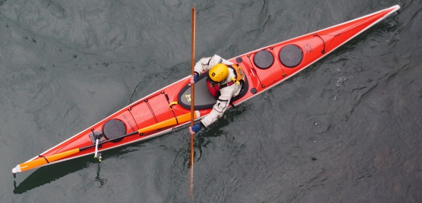 A man in a yellow helmet paddling a long red kayak in the water