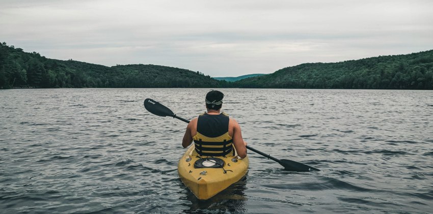 A man paddling a yellow kayak on the wavy water