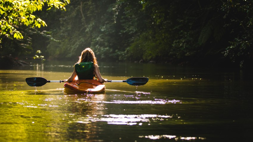 A woman sitting in an orange kayak holding a paddle on the water