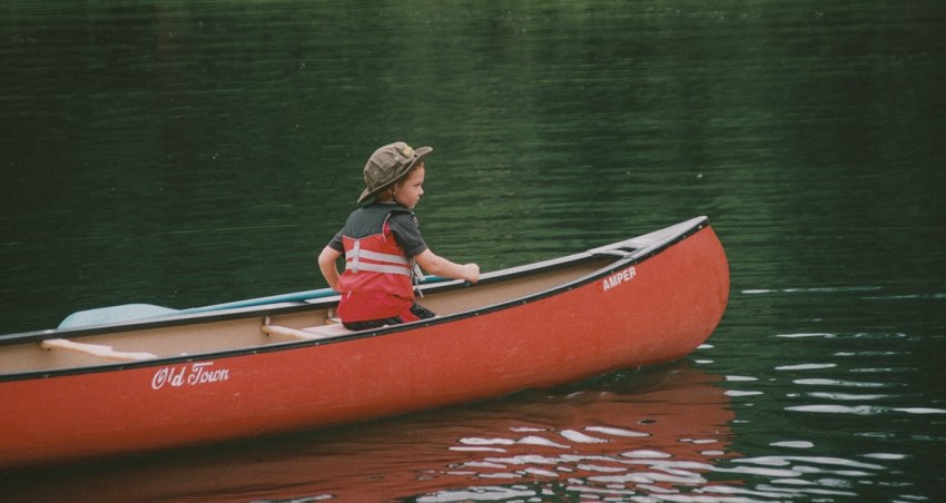 A kid sits in a red canoe on the water