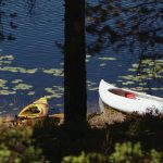 A yellow kayak and a white canoe by the lake