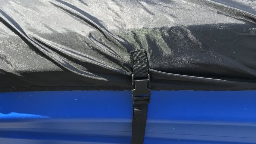 Black polyester cover strapped to the top of a blue kayak