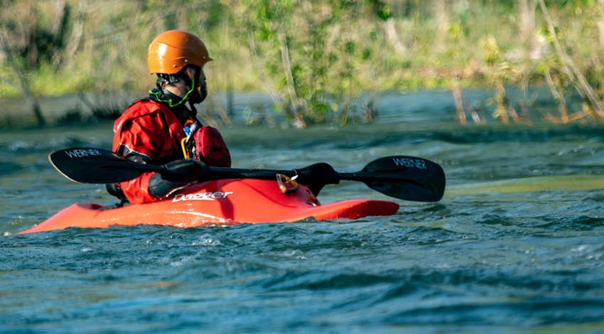 A man wearing an orange helmet and a red life vest sits in a red kayak on the water