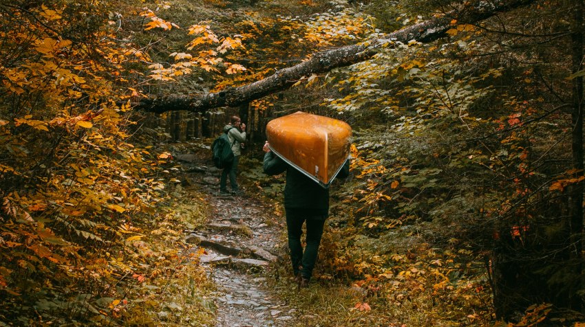 A man portages his orange kayak through the autumn wood 