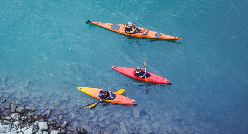 A man and two kids paddling their kayaks on the water