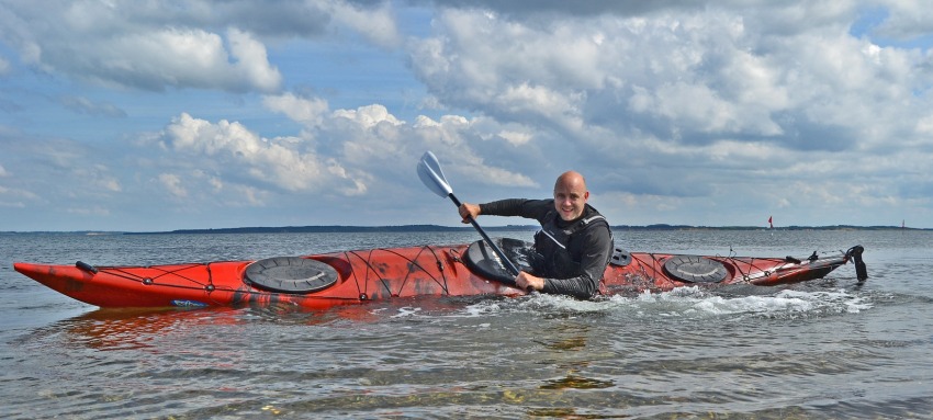 A man edging his long red kayak on the water