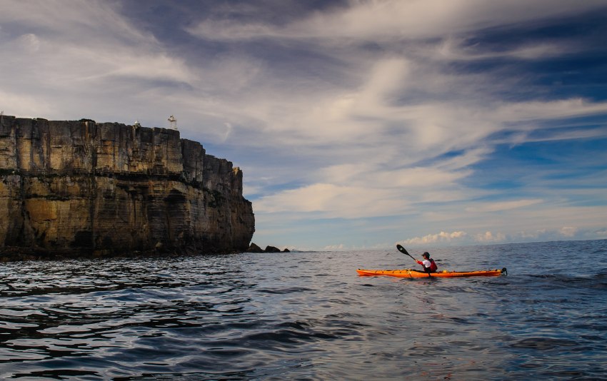 A man paddling an orange kayak in the costal waters