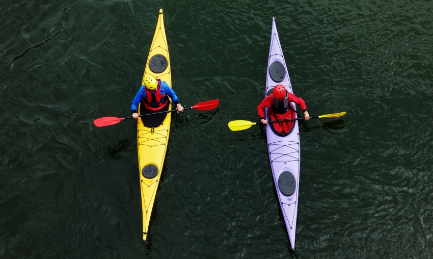 Two men sitting in their long kayaks on the water