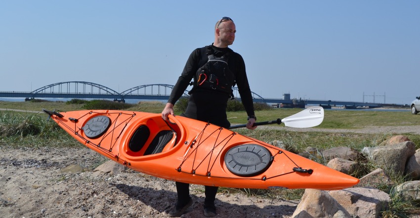 A man carrying a long red kayak and a white paddle
