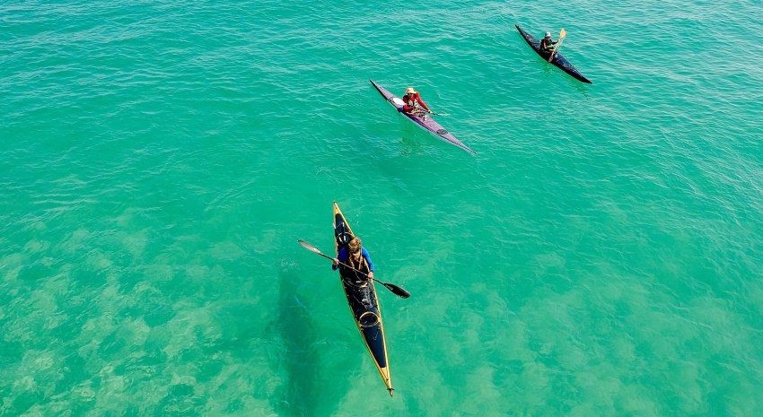 Three people paddling their long touring kayaks in the cyan waters