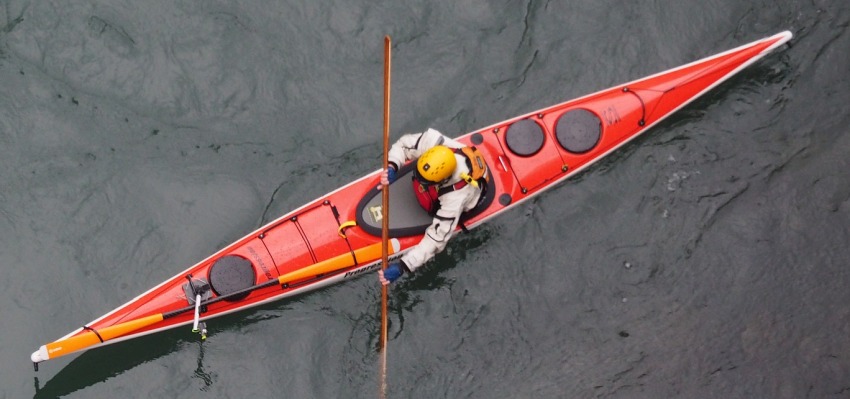 A man in a yellow helmet paddling a long red kayak on the water